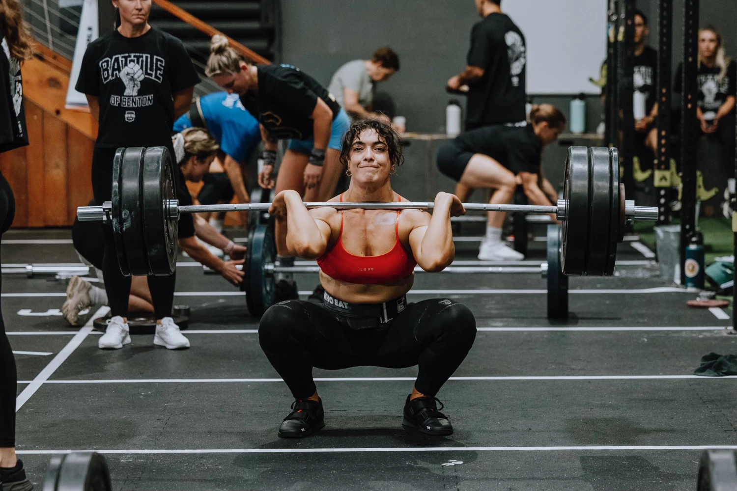 An athlete front squatting on a marked competition lane, with a judge alongside